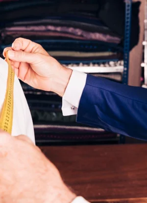 A professional tailor adjusting the fit of a men's garment, ensuring precision and style with FCOM India’s specialized tailoring services